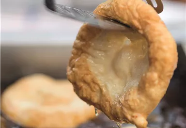 Ein gebackenes Gebäck wird mit einem Spatel aus heißem Öl gehoben. Es hat eine goldbraune Farbe und sieht sehr appetitlich aus.