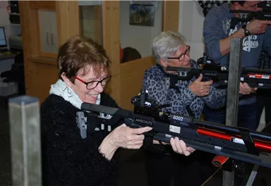 Zwei Frauen stehen in einem Schießstand und zielen mit Luftgewehren. Beide haben konzentrierte Ausdrücke und tragen Schutzbrillen.