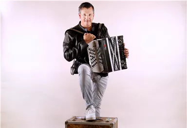 Eine Gruppe von sieben Musikern steht auf einer Bühne. Sie lächeln und posieren vor einem festlichen Hintergrund mit blauen Lichtern.