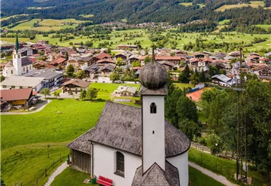 A picturesque church on a hill with a beautiful mountain landscape in the background. The surroundings are green and idyllic, with a small village nearby.