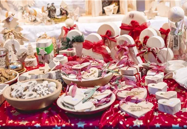 A festive table with handmade gifts and decorations. The objects are in various shapes and colors, surrounded by red fabric with stars.