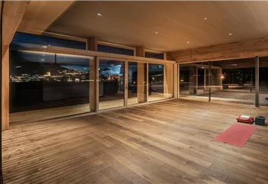 A modern, bright room with large windows and wooden flooring. It offers a view of the city and is ideal for relaxation or yoga.
