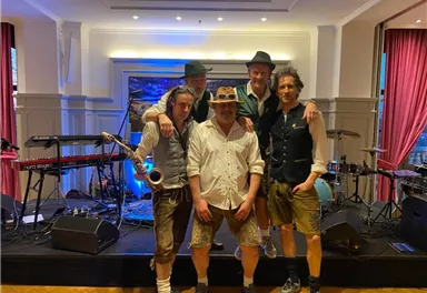 Eine Band steht auf der Bühne, umgeben von Musikinstrumenten. Sie tragen traditionelle Kleidung und posieren für das Foto.