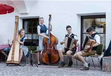 Eine Gruppe von vier Musikern spielt traditionelle Musik in einem malerischen Innenhof. Zu sehen sind eine Harfe, ein Kontrabass und zwei Akkordeons.