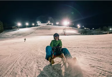 Eine nächtliche Skisession auf einer beleuchteten Piste. Skifahrer fahren den Hang hinunter, während die Lichter die Landschaft erhellen.