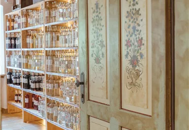 Eine holztür mit dekorativen Blumen und eine Regale mit zahlreichen Flaschen im Hintergrund. Der Raum wirkt einladend und geschmackvoll eingerichtet.