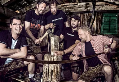 A group of five men is working together to process wood. They are in a rustic environment with wooden elements.
