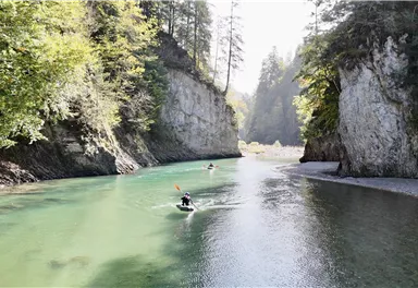 Ein schöner Fluss, umgeben von hohen Felsen und Bäumen. Zwei Personen paddeln im Wasser.