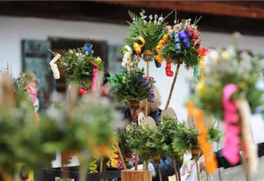 Colorful, decorated bouquets with flowers and colored ribbons are on a table. In the background, there are people and a traditional building.