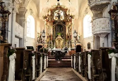 Eine prächtige Kirche mit einer kunstvoll gestalteten Innenausstattung. Der Blick führt den langen Weg zum Altar, umgeben von eleganten Sitzbänken.