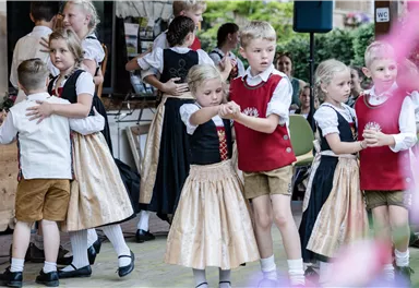 Eine Gruppe von Kindern tanzt in traditioneller Tracht. Sie zeigen fröhliche Bewegungen und haben viel Spaß zusammen.