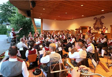 A brass music ensemble is playing on a stage. The conductor leads the orchestra while the musicians concentrate on performing in traditional attire.