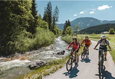 Ein natürlicher Felsen mit einer Öffnung, die einen Blick auf einen ruhigen See und Hügel gewähren. Der Himmel ist klar und blau.