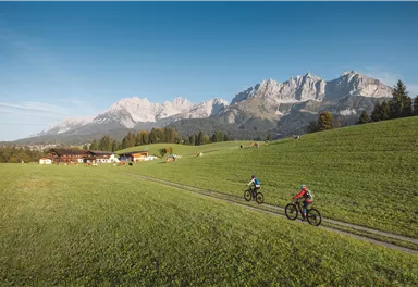 Eine schneebedeckte Straße mit hohen Schneewänden und einem Holzhaus in der Nähe. Der Himmel ist klar und blau mit einigen Wolken.