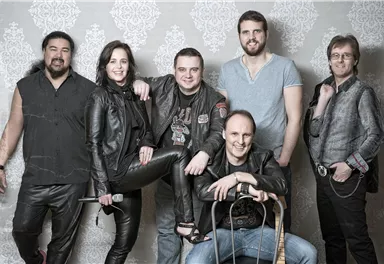 A band consists of six members posing in casual clothing. The background is bright and decorative.