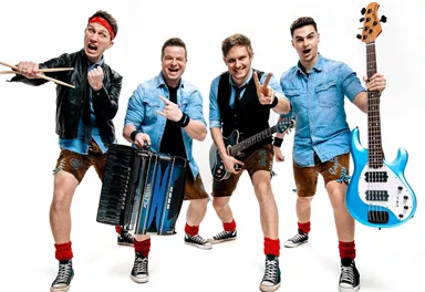 Eine fröhliche Band mit fünf Mitgliedern posiert in einer Action-Haltung. Sie tragen Trachtenlooks und halten verschiedene Musikinstrumente in der Hand.
