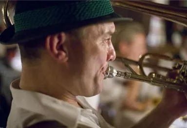 Ein Musiker spielt Trompete in einem gemütlichen Ambiente. Er trägt einen Hut und konzentriert sich auf die Musik.