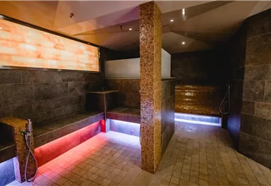 Ein moderner Wellnessbereich mit großen Fliesen und sanfter Beleuchtung. Dusch- und Entspannungsbereiche sind harmonisch gestaltet.