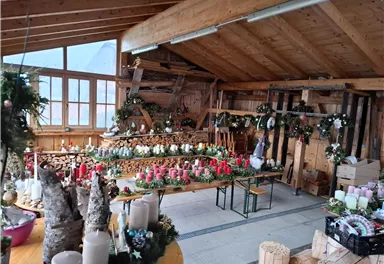 Ein gemütlicher Raum mit Holzdekor, geschmückt für die Weihnachtszeit. Auf Tischen stehen viele Kerzen und festliche Dekorationen.