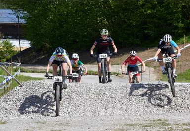 Fünf Radfahrer fahren über einen Schotterhindernis im Gelände. Die Fahrer tragen Rennkleidung und Helme.