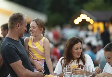 Eine fröhliche Familie sitzt zusammen und genießt ein Essen. Kinder lachen und haben Spaß miteinander.