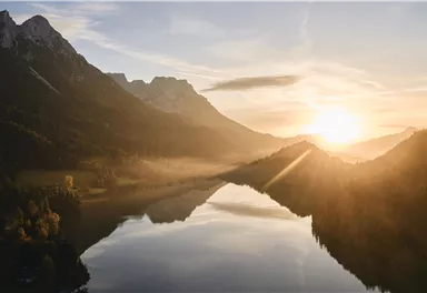 A picturesque sunrise over a tranquil lake, surrounded by mountains. The gentle rays of light reflect off the water.