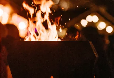 A fire bowl with blazing flames and sparks. Blurred lights can be seen in the background.