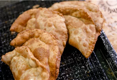 Frittierte Teigtaschen auf einem Gitter. Sie sind goldbraun und knusprig, ideal als Snack.