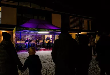 Eine Live-Musikaufführung unter einem Zelt in der Nacht. Die Zuschauer stehen im Schnee und genießen die Musik.