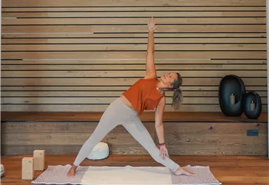 Eine Frau macht eine Yoga-Pose in einem hellen, modernen Raum. Die Holzwände und Matten schaffen eine entspannende Atmosphäre.