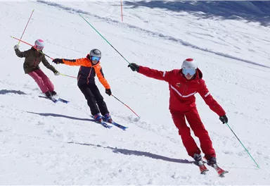 Drei Skifahrer fahren die Piste hinunter. Sie tragen helle Skikleidung und genießen den Schnee.