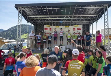 A group of athletes stands on a stage at an awards ceremony. In the foreground, many spectators are visible, watching the event.