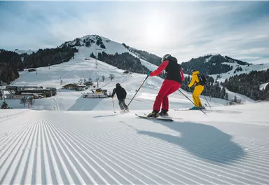 Three skiers are skiing down the snowy slope. In the background, snow-covered mountains and a clear winter landscape can be seen.