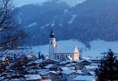 A picturesque winter landscape with a church in the foreground and snow-covered mountains in the background. The tranquil scene radiates peace and cold.
