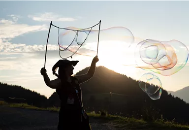 Eine Person steht im Sonnenuntergang und bläst Seifenblasen. Die Berge und der Himmel sind im Hintergrund gut sichtbar.
