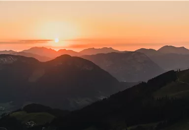 Ein atemberaubender Sonnenuntergang über den Bergen. Die Silhouetten der Gipfel heben sich gegen den bunten Himmel ab.