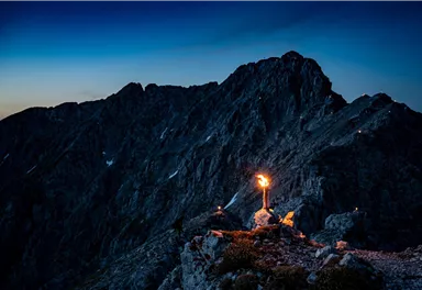 An impressive mountain landscape at twilight. A torch illuminates the foreground and lights up the rocky surroundings.
