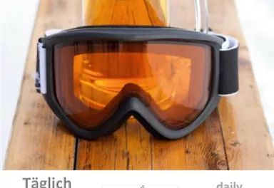A beer glass is on a wooden table next to a ski goggles. Above it is the announcement of a daily après-ski party with a DJ.