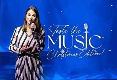 Eine Frau steht auf der Bühne und singt in ein Mikrofon. Im Hintergrund ist eine festliche Weihnachtsdekoration zu sehen.