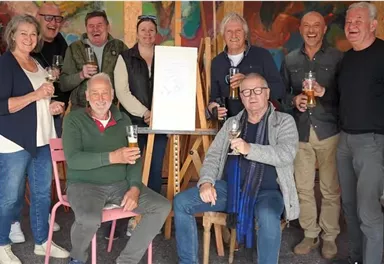 A group of people stands and sits together, holding glasses in their hands. They are smiling and seem to be enjoying a celebration or an important event.