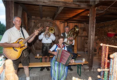 A group of musicians plays traditional instruments in a rustic setting. The performance takes place in a wooden building, surrounded by decorative elements.