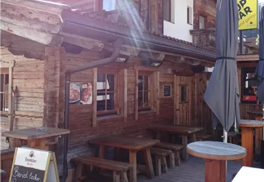 Eine gemütliche Bar im alpinen Stil mit Holzverkleidung und Außenterrasse. Über der Bar hängen große Schilder mit der Aufschrift „TOP BAR“.