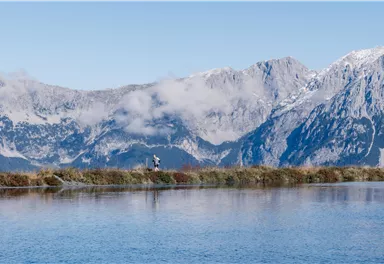 Ein stiller See umgeben von majestätischen Bergen und Wolken. Die Landschaft strahlt Ruhe und natürliche Schönheit aus.