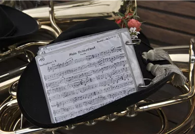 A black hat with sheet music lies on a musical instrument. The notes show a piece called "My Homeland".