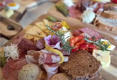 Ein ansprechendes Käse- und Wurstbrett mit verschiedenen Brotsorten und frischen Zutaten. Bunte Blüten und Kräuter verleihen dem Arrangement zusätzlichen Charme.