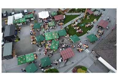Ein belebter Markt mit vielen Ständen und grünen Pavillons. Viele Menschen sitzen zusammen und genießen die Atmosphäre.