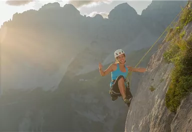 Eine Person klettert an einer steilen Felswand in den Bergen. Die Szene wird von Sonnenlicht erleuchtet und zeigt die Freude des Kletterns.