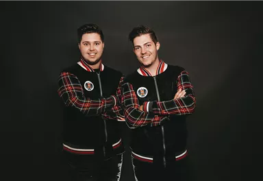 Ein lächelnder Mann steht an einer Säule mit gekreuzten Armen. Er trägt einen blauen Anzug und wirkt selbstbewusst und freundlich.