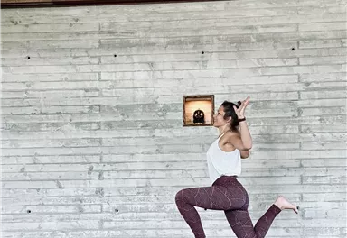 Eine Person übt Yoga in einer modernen Umgebung mit Holz- und Betonwänden. Sie zeigt eine dehnbare Pose auf einer Matte.