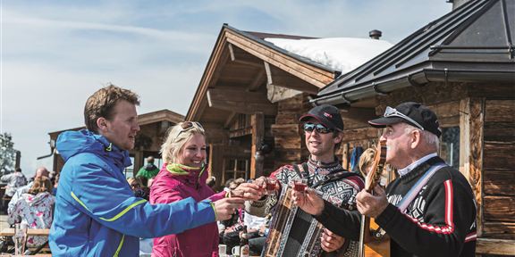 Eine Gruppe von Freunden stößt mit Biergläsern an. Sie sitzen an einem Tisch und genießen die gemeinsame Zeit in einer gemütlichen Umgebung.